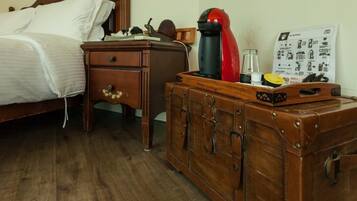 A wooden bed with white linens, a small wooden nightstand with a lamp, and a vintage suitcase on a wooden dresser.