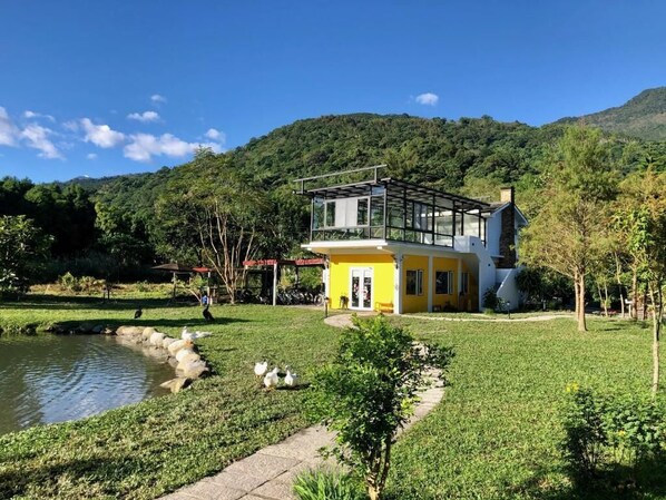 Une maison à deux étages dotée d’un balcon, entourée d’un jardin bien entretenu et d’un étang.