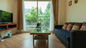 Un salón con televisor, una mesa de centro de vidrio, un sofá con cojines estampados y vistas a la vegetación a través de una puerta corrediza de vidrio.