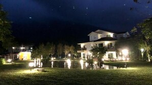 Una casa de dos pisos con un patio delantero bien iluminado y un pequeño estanque.