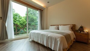 Un dormitorio con una cama grande, piso de madera, una mesita de noche con lámpara y vista a la vegetación a través de una puerta corredera.
