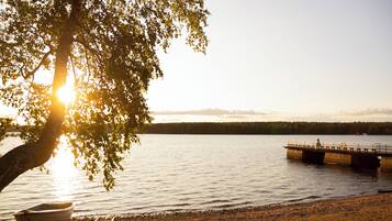 A boat docked near a tree by a calm lake with a pier in the background.