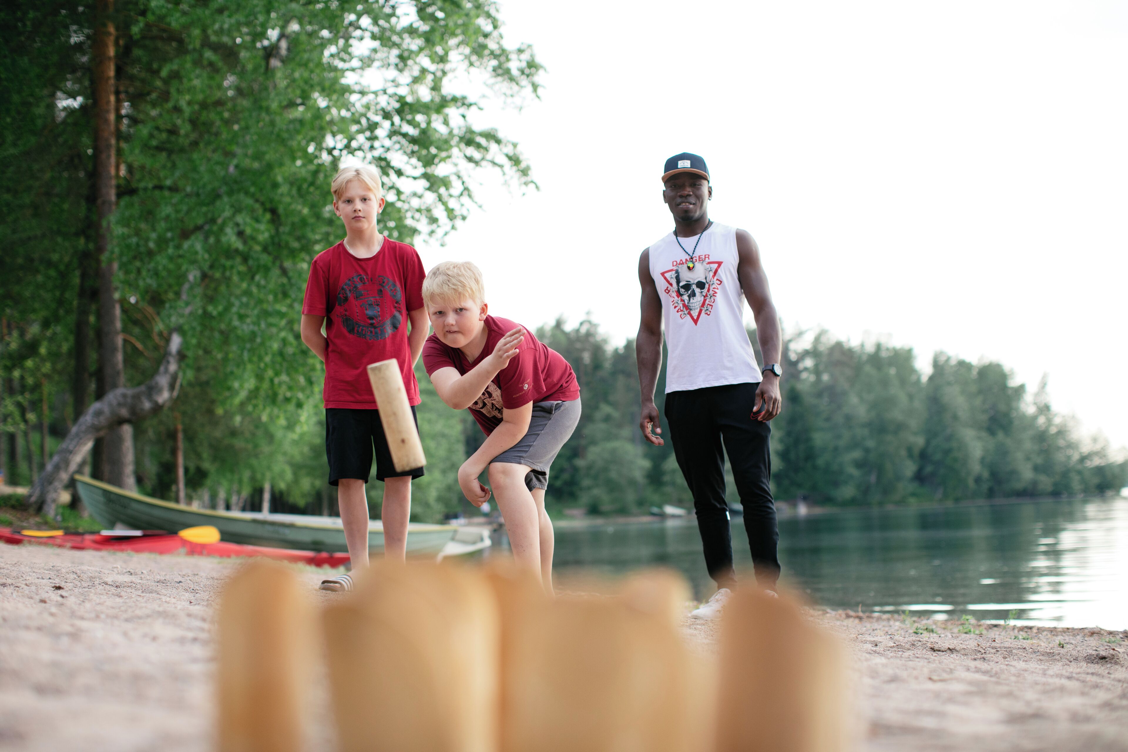 Three people standing on a sandy beach with a lake in the background.