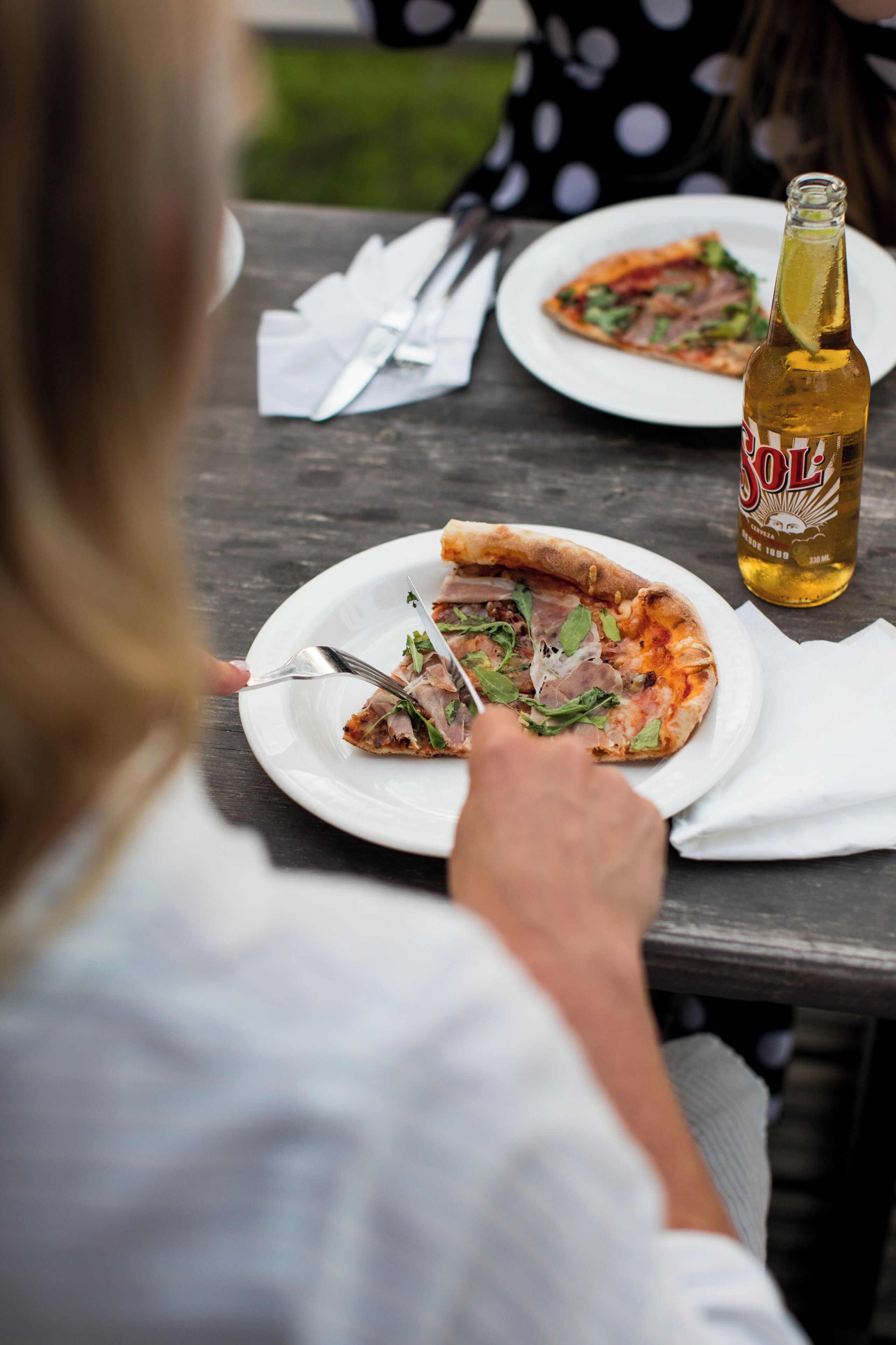 Una mesa de comedor con pizza, una botella de cerveza Sol y una persona comiendo.
