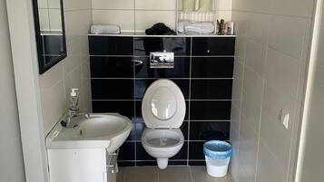 Pieni kylpyhuone, jossa on valkoinen pesuallas, mustat laatat seinissä, wc ja sininen pyykkikori.