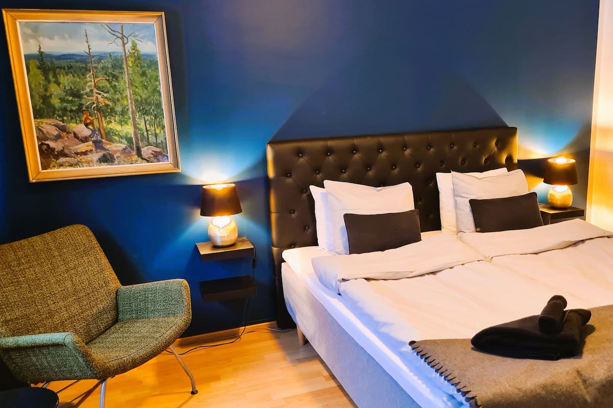 A bedroom with a large bed, two bedside tables with lamps, a chair, and a painting on the wall.