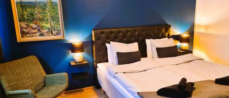A bedroom with a large bed, two bedside tables with lamps, a chair, and a painting on the wall.
