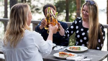 Three people sitting at a wooden table outdoors, enjoying drinks and food.