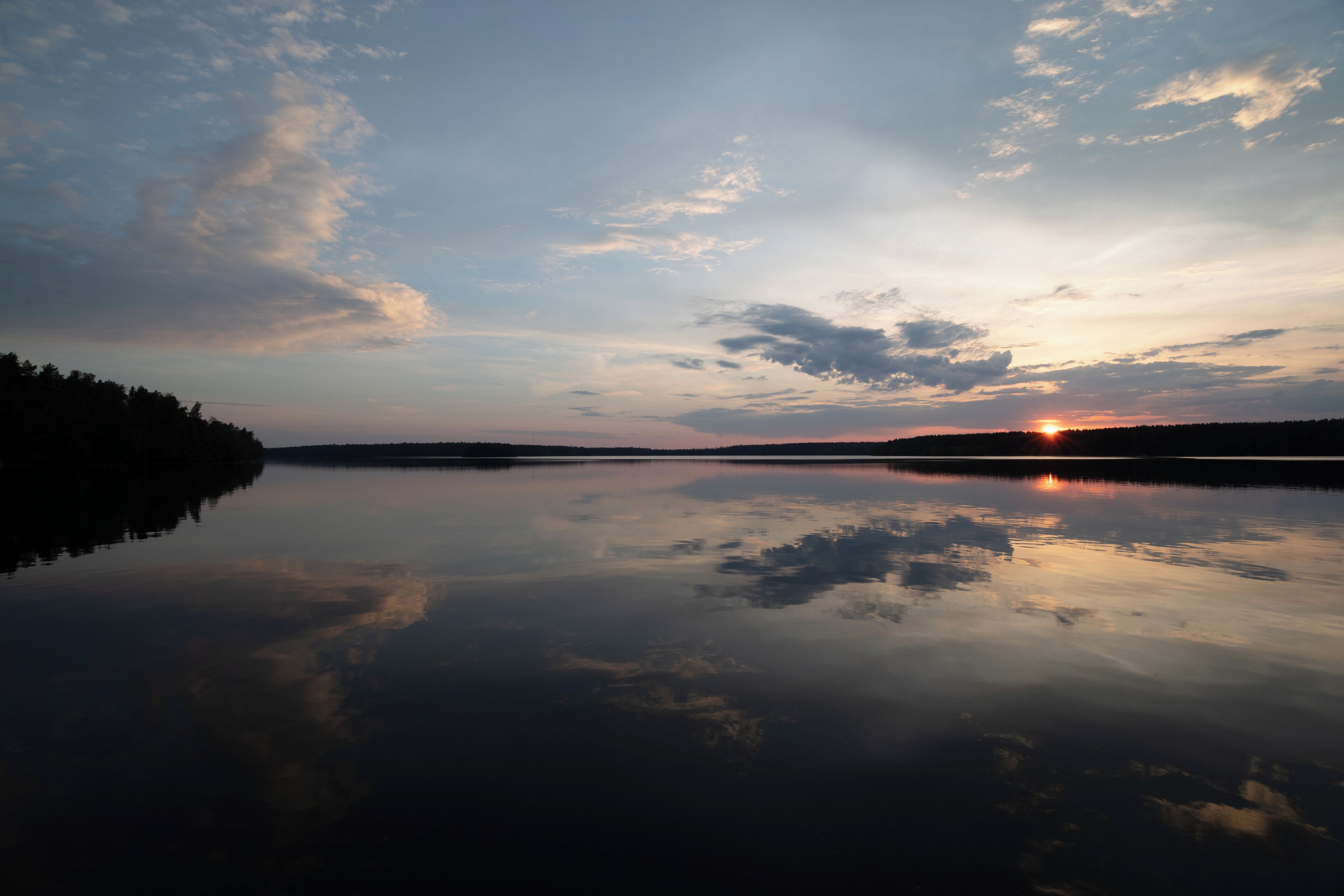 Un llac tranquil a la posta de sol amb un reflex clar del cel i del sol.
