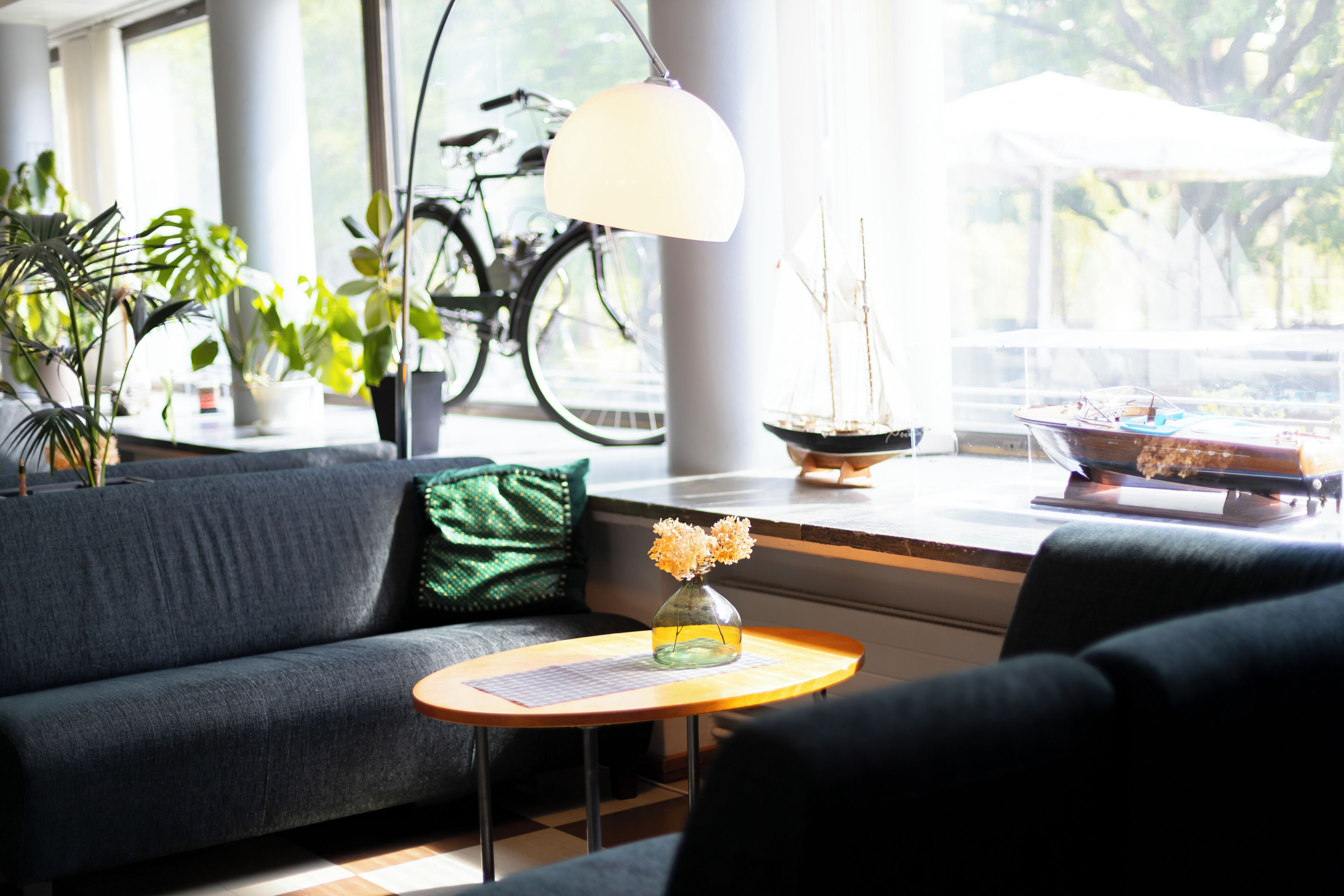 A modern living room with a sofa, a small round table with a vase of flowers, a bicycle, and a sailboat model.