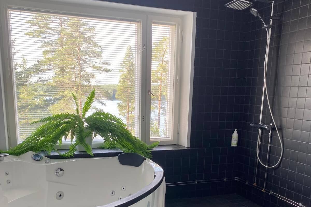 A modern bathroom with a white jacuzzi tub, a shower, and a large window with blinds.