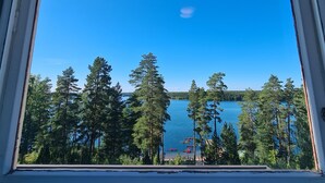 Vista de un lago rodeado de altos árboles, con cielo despejado y un pequeño bote visible en el agua.