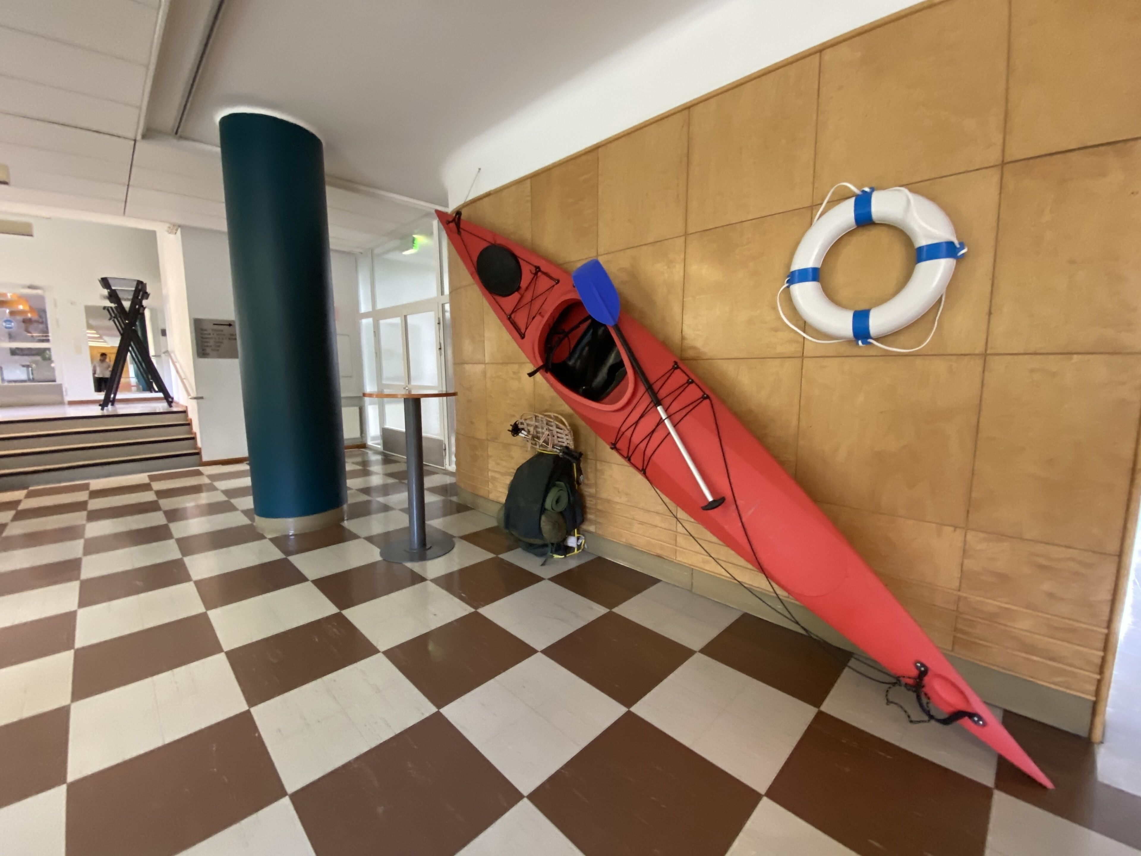 Um caiaque vermelho encostado em uma parede, com um flutuador por perto.