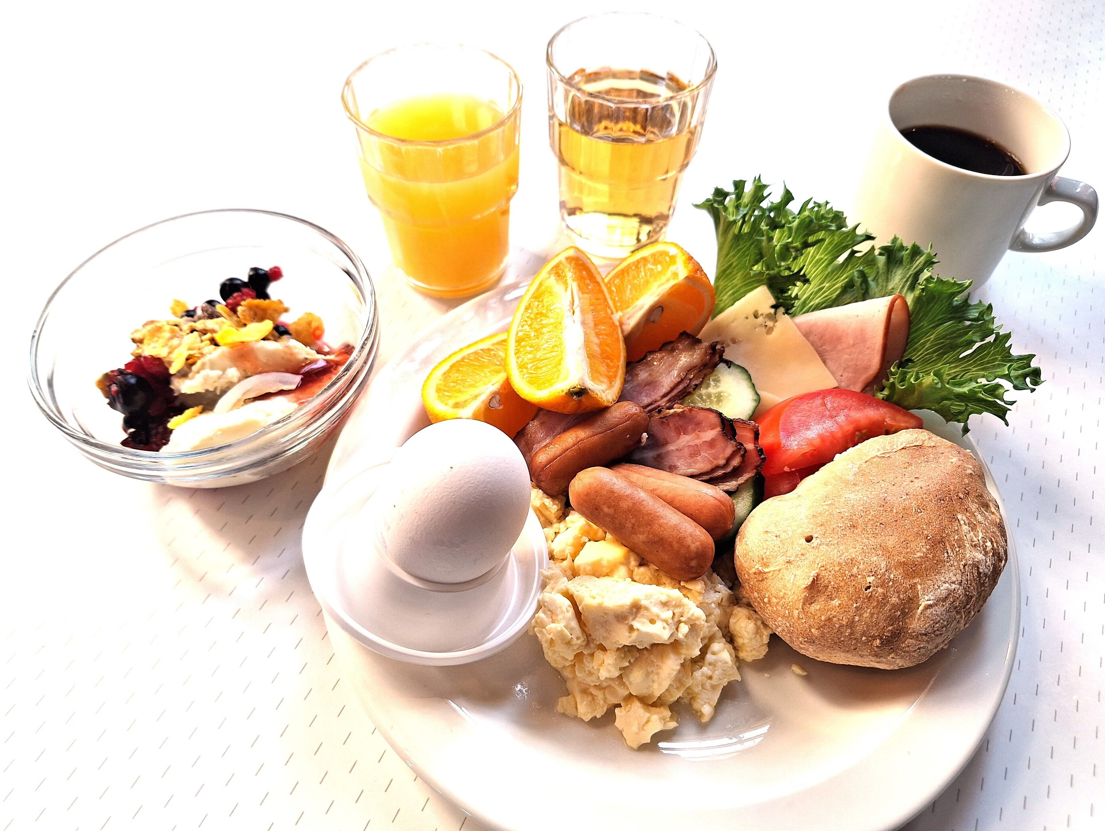 Een ontbijtbord met roerei, worst, ham, toast, en een portie fruit en groenten.
