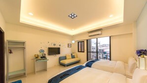 Habitació d'hotel amb dos llits, un sofà, una televisió, un escriptori i una finestra amb vista a la ciutat.