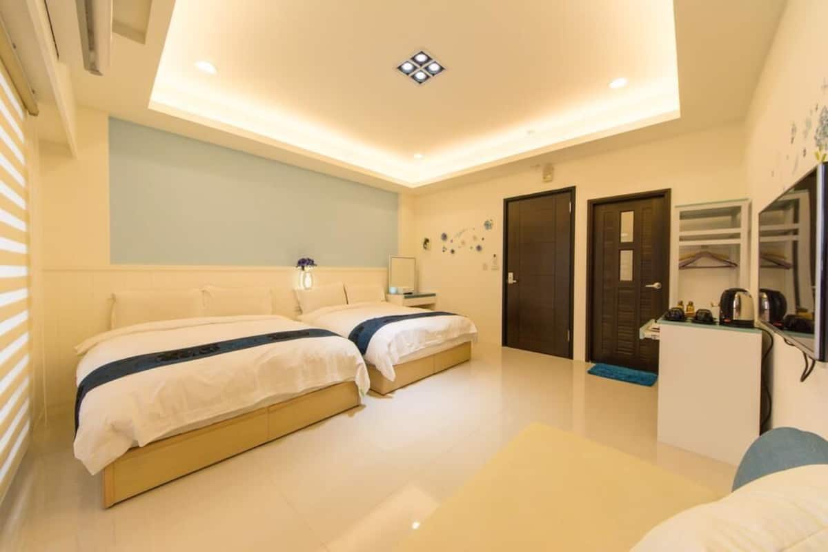 A modern hotel room with two beds, a desk, a mirror, and a wardrobe.