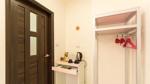 Habitació d'hotel amb una porta de fusta, un petit escriptori blanc amb una paperera i un armari amb penjadors vermells.