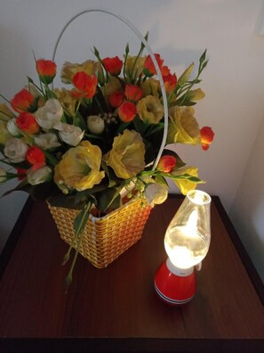 A wicker basket containing artificial flowers and a red lamp on a wooden table. - Nghi An House (Da Lat)