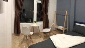 Una habitación de hotel con una cama, una mesita con sillas, una ventana con cortinas y una silla colgante de madera.