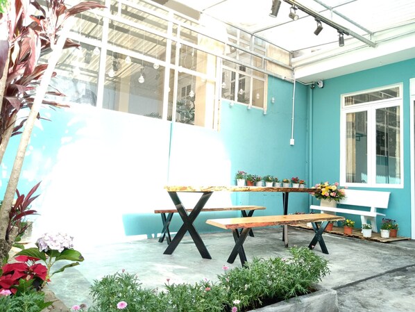 An outdoor seating area with wooden benches and tables, surrounded by potted plants and flowers. - Nghi An House (Da Lat)