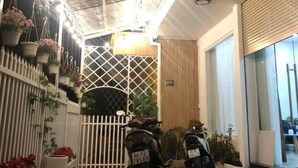 Un espacio exterior techado con dos scooters estacionados, una cerca blanca y macetas colgantes con flores.