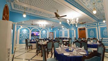 A dining area with blue and white decor, chandeliers, and ceiling fans. Tables are set with white tablecloths and chairs.
