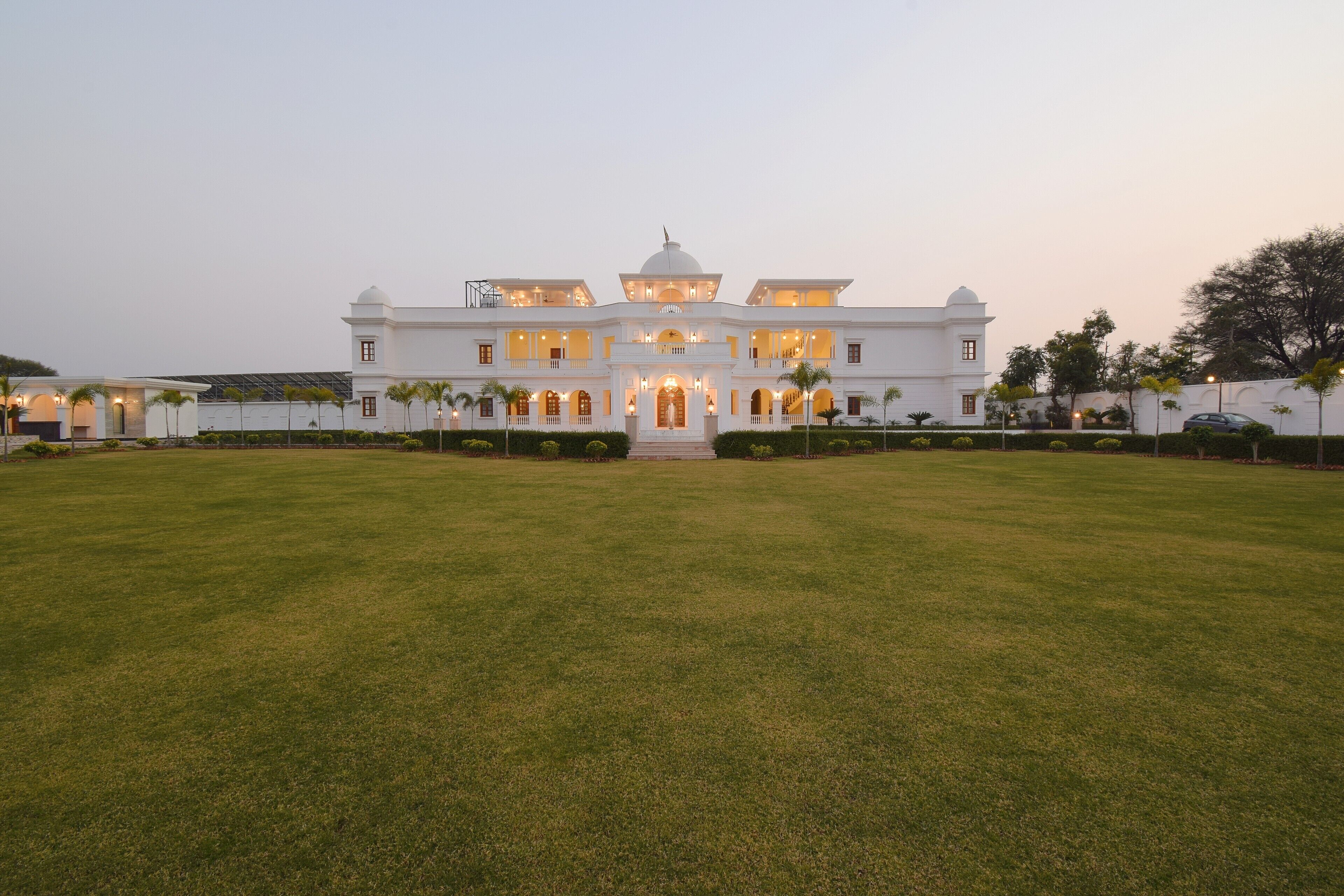A large, white building with a central dome and multiple balconies, surrounded by a well-maintained lawn.