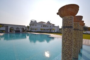 A swimming pool with a white building in the background. - Umaid Farm Resort - A Legacy Vintage Stay in Jaipur (Jalsu)