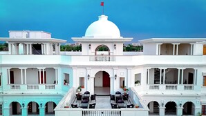 A multi-story building with a central dome, balconies, and a flag on top. - Umaid Farm Resort - A Legacy Vintage Stay in Jaipur (Jalsu)