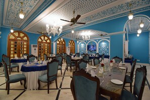 A banquet hall with blue walls, chandeliers, and wooden tables set for dining. - Umaid Farm Resort - A Legacy Vintage Stay in Jaipur (Jalsu)