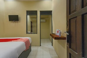 A hotel room with a bed, a TV mounted on the wall, a mirror, and a door leading to another room.