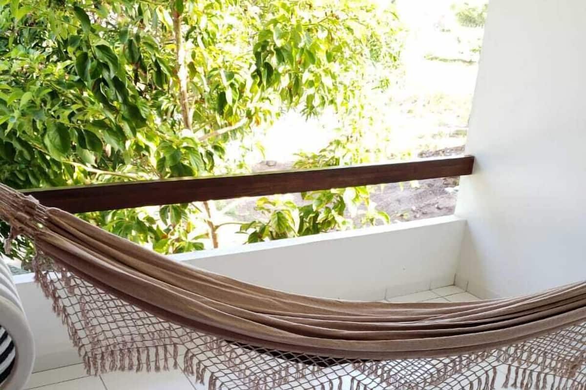 Uma rede numa varanda com vista para árvores e um chão de azulejos brancos.