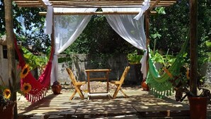 Une terrasse en bois avec une table et des chaises, entourée d’une pergola agrémentée de rideaux blancs.