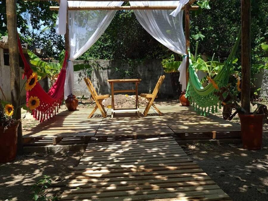 Un terrazzo in legno con tavolo e sedie, circondato da un pergolato con tende bianche.