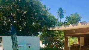 Une piscine avec une terrasse carrelée, un espace salon couvert et un jardin clôturé.