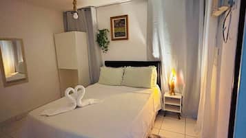 A bedroom with a bed, a bedside table with a lamp, a mirror, and a framed picture on the wall.