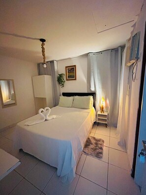 Een slaapkamer met een bed, een nachtkastje met een lamp, een spiegel en een lijst met een foto aan de muur.