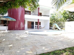 Un bâtiment à deux étages, avec une façade recouverte de tuiles, une piscine et un hamac.