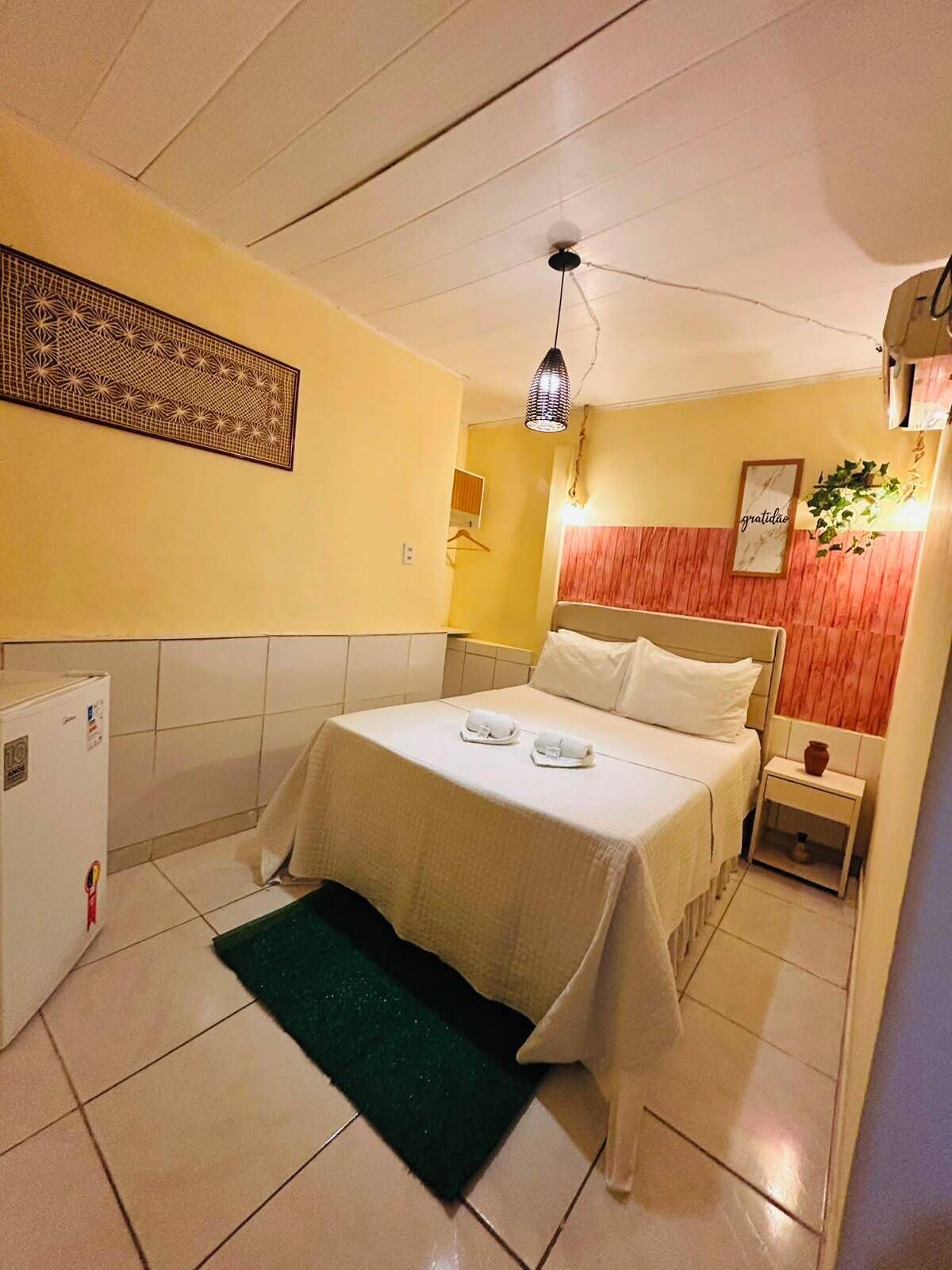 A hotel room with a bed, a nightstand, a wall-mounted artwork, a ceiling fan, and a small plant.