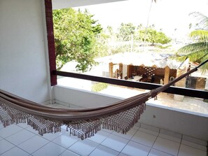 Un hamac sur un balcon avec vue sur un immeuble et des arbres.