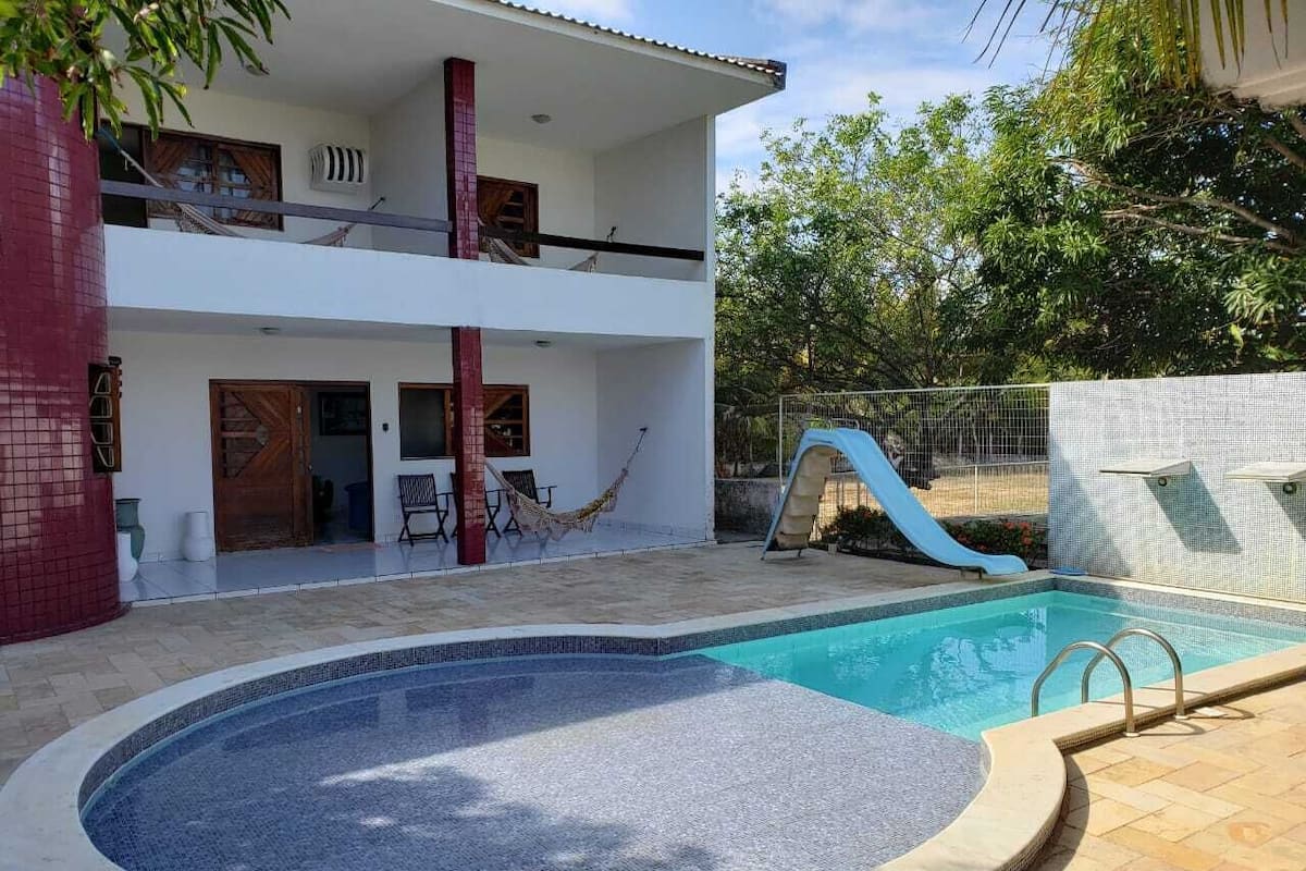Uma casa de dois andares com piscina, escorrega e rede.