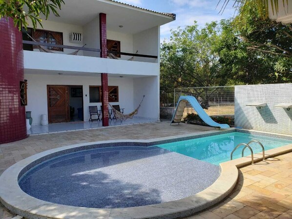 Une maison à deux étages avec une piscine, un toboggan et un hamac.
