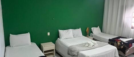 A hotel room with two beds, a green accent wall, a window with curtains, and a tiled floor.