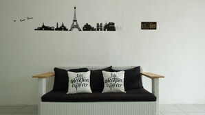 A white wicker sofa with black cushions and two pillows with the text "I love Paris" and "I am a dream explorer."