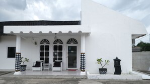 A white building with a covered entrance, two potted plants, a black lantern, and a checkered column.