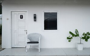 A white door with a number plate, a wicker chair, a window, and a potted plant. - OYO 2557 The Apple Residence (Pangkalpinang)