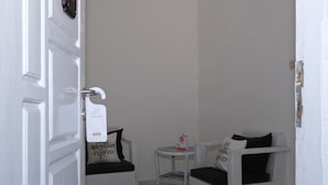A clean, white room with two wicker chairs, one with a cushion and a sign, and a small table with a sign.