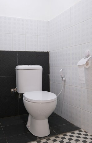 A bathroom with a toilet, a toilet paper holder, and a black and white checkered floor. - OYO 2557 The Apple Residence (Pangkalpinang)