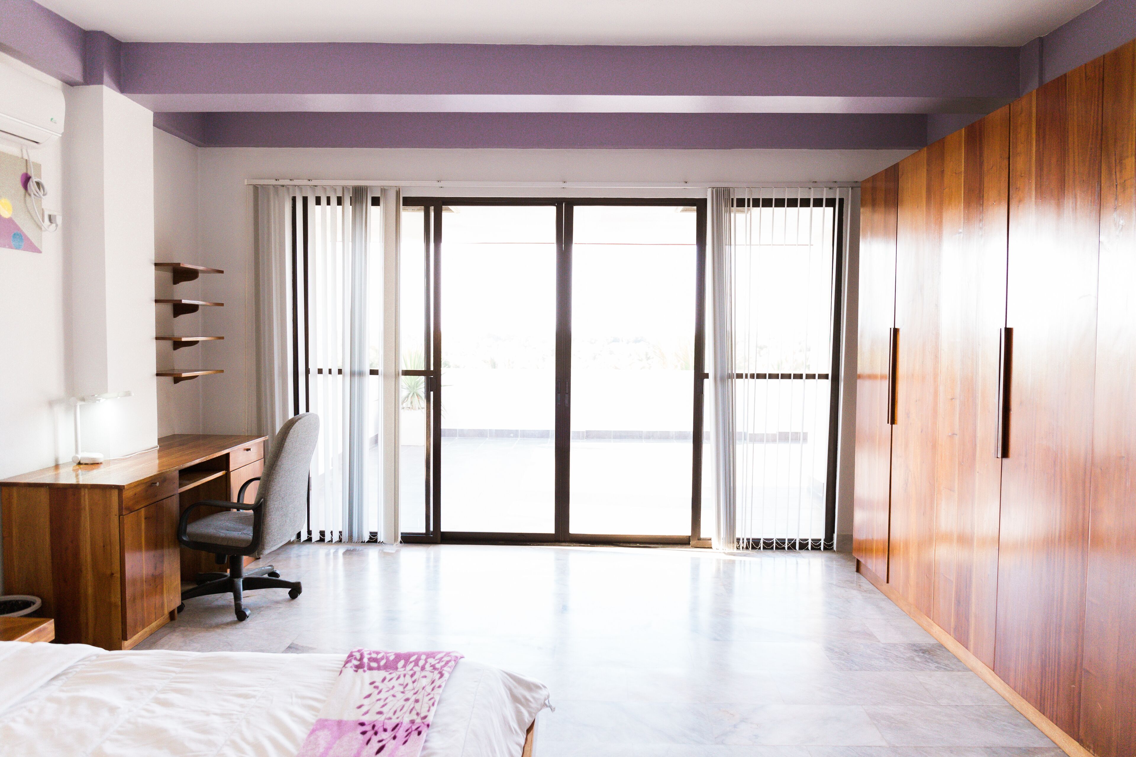 Un dormitorio con cama, escritorio, silla, armario y puertas de cristal correderas grandes.