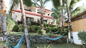 A hammock in a lush garden with a building in the background. - Seaview Hills Luxury Apartments & Rooms (Dauis)